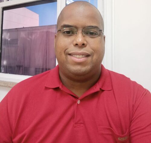 Homem com camisa vermelha, pele negra, cabelo raspado.